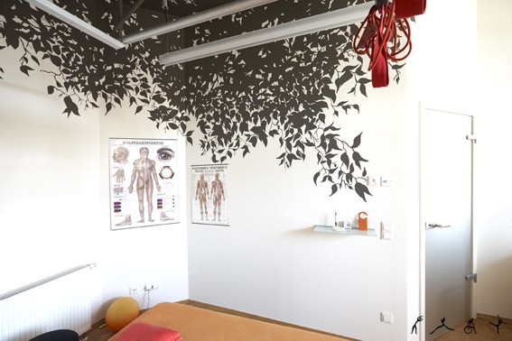 Heller Physiotherapie-Behandlungsraum mit Anatomiepostern, Wanddeko und Gymnastikball.